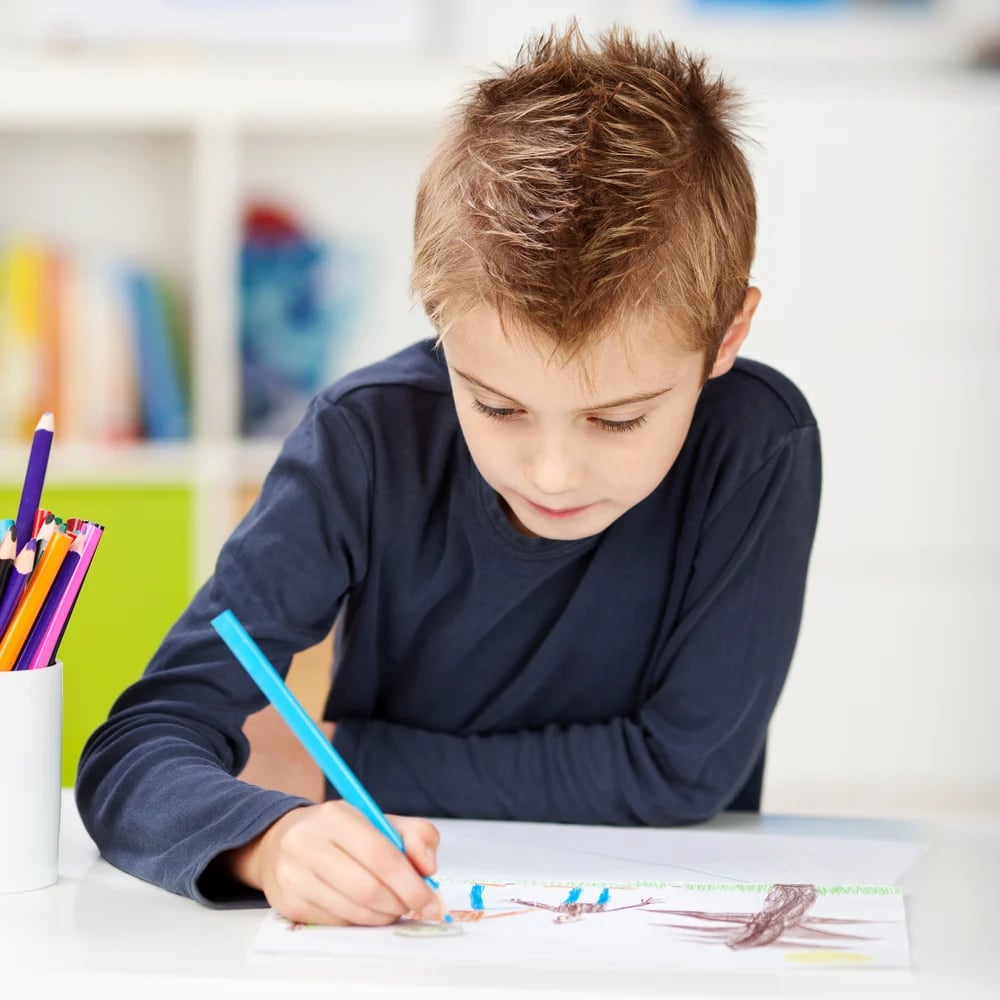 Little boy using colored pencil while drawing on paper at table in house