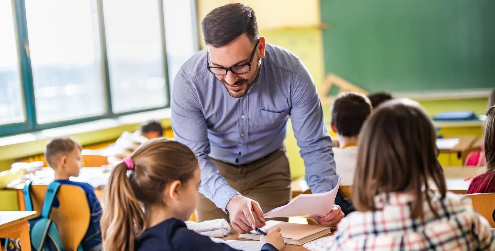 Male teacher bending over desk to help student